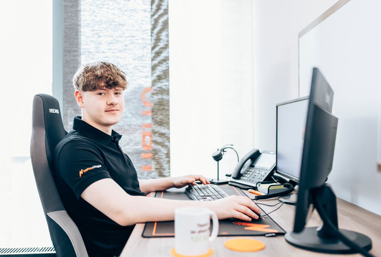 Mitarbeiter von nano itdesign arbeitet an einem Arbeitsplatz mit zwei Bildschirmen, Headset und Telefon